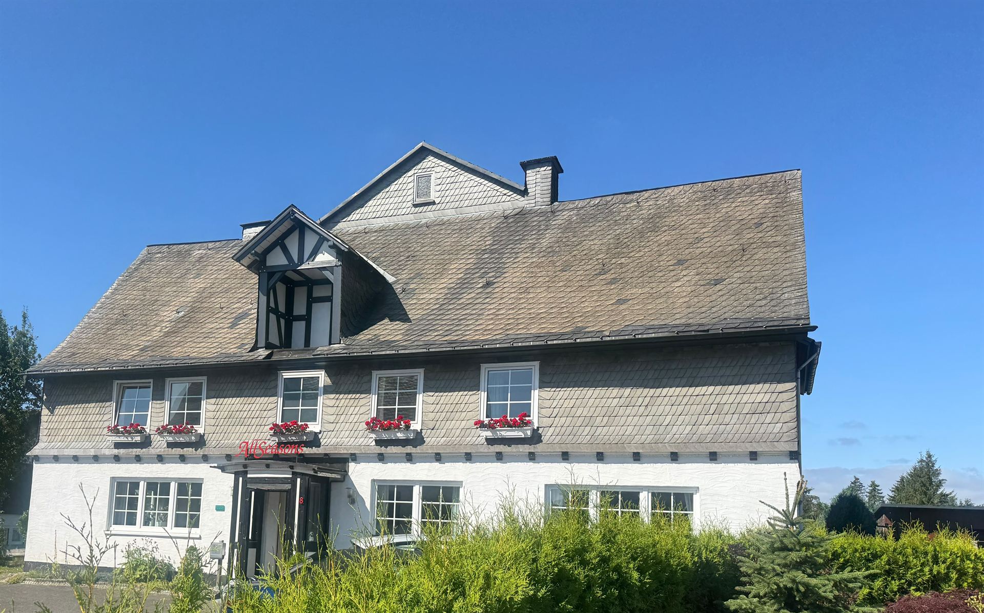 Haus Astenalm in der Sommersonne mit blühenden Geranien an der Schieferfassade